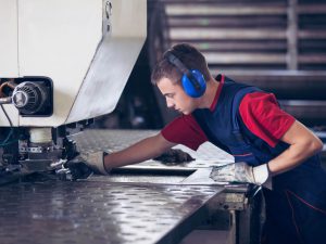 In einer Fabrik arbeitet Industriearbeiter in der Metallpresse, die ein bearbeitbares Stahlstück hält.