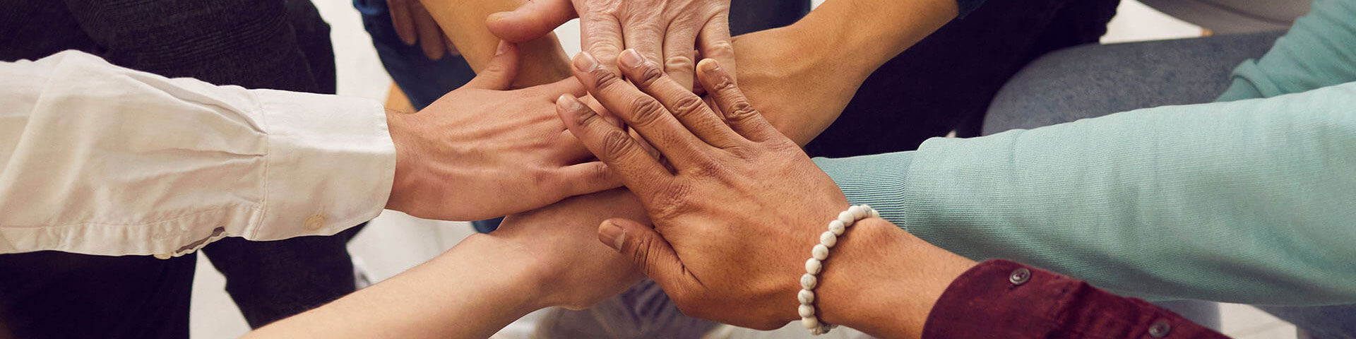 Menschen unterschiedlichen Alters und Nationalitäten legen ihre Hände übereinander und symbolisieren ihre Einheit und Unterstützung. Team von Menschen, die für produktive Arbeit und ein positives Ergebnis eingerichtet sind.