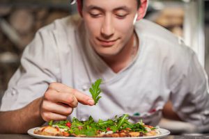 junger männlicher Koch, der mit Kräutern auf weißem Teller köstlichen Vorspeise zubereitet