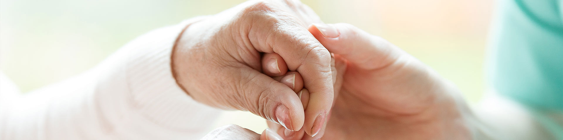 Pflegerin hällt Hände einer älteren Frau